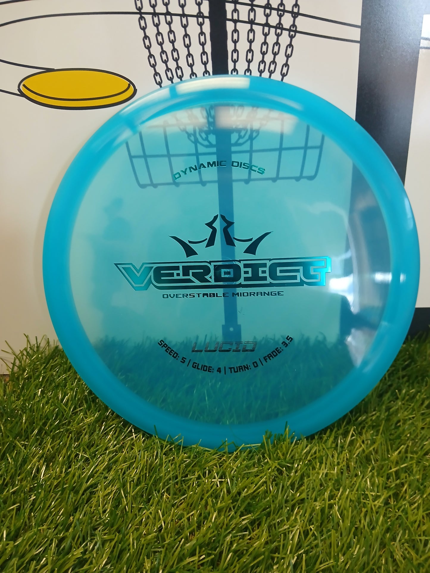 Blue Dynamic Discs Verdict overstable midrange disc on grass with basket background