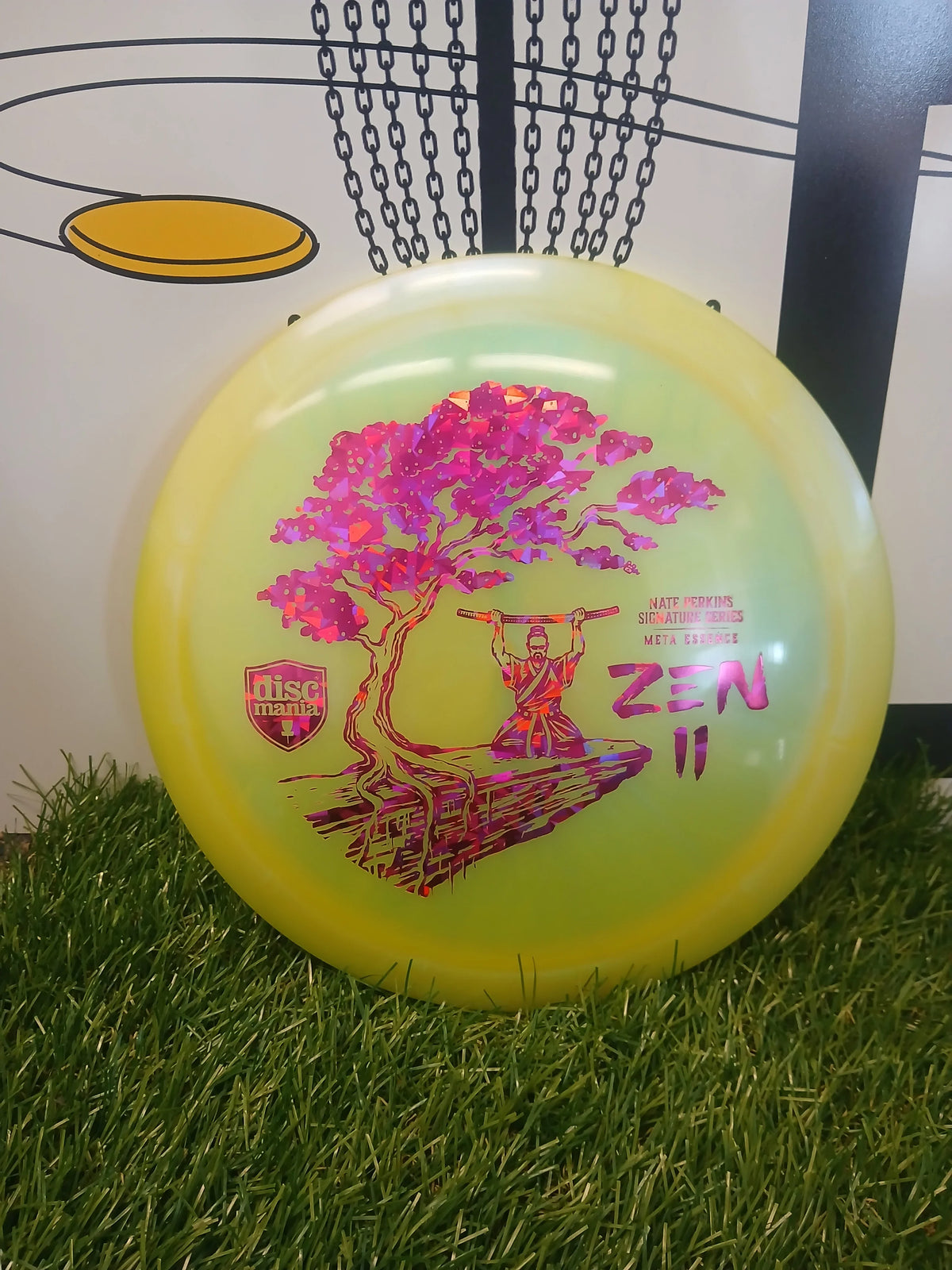 Discmania Zen II disc golf disc with pink tree design, Nate Perkins Signature Series, on grass near basket