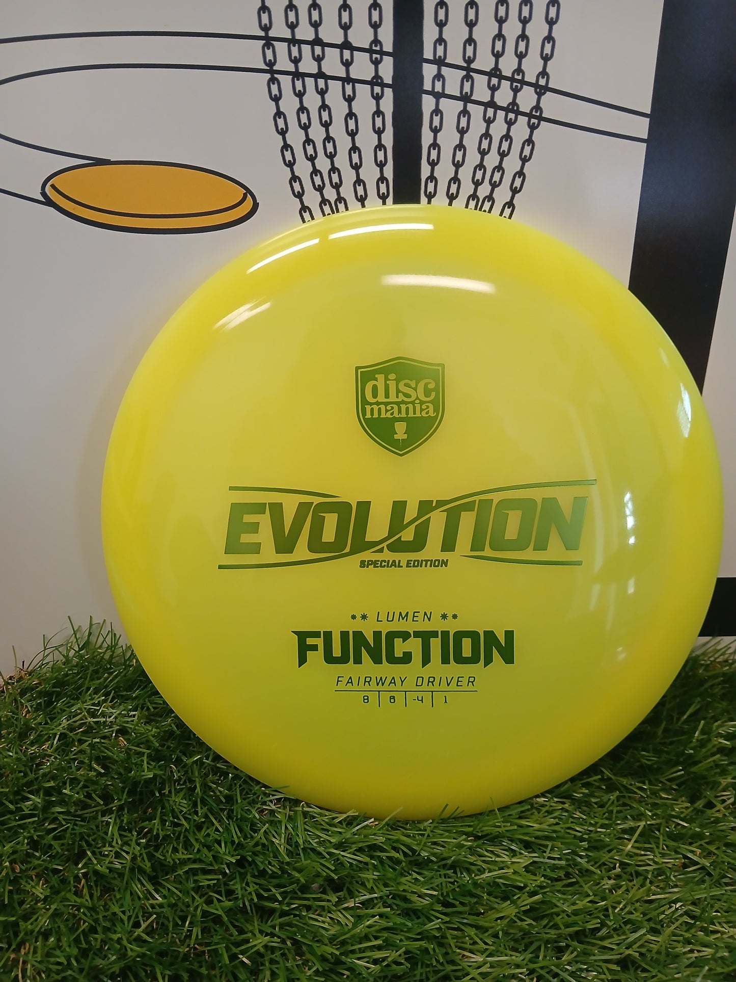 Bright yellow Discmania Evolution Function fairway driver disc on artificial grass, ideal for disc golf enthusiasts.
