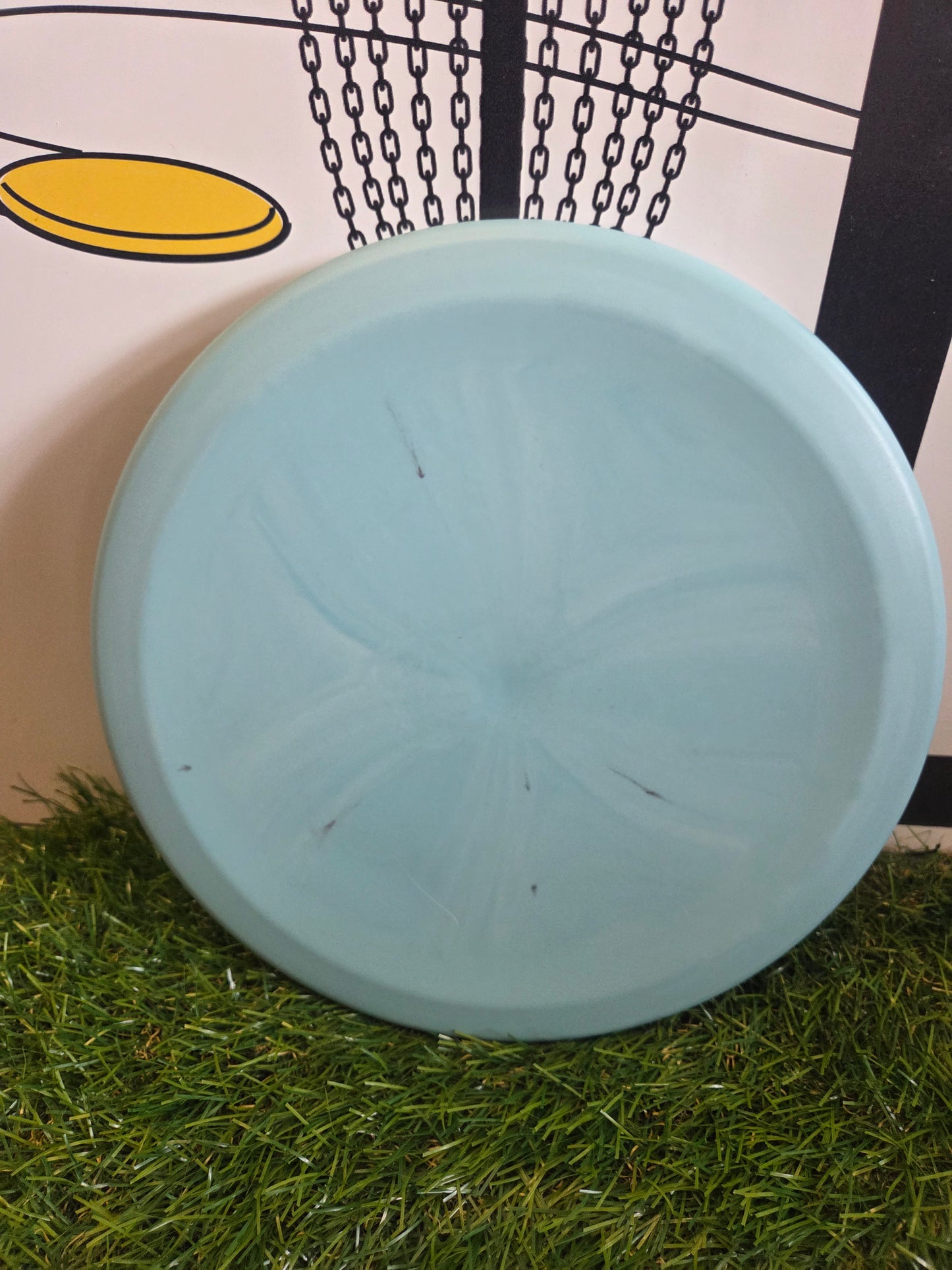 Light blue disc golf disc on artificial grass with chain basket background