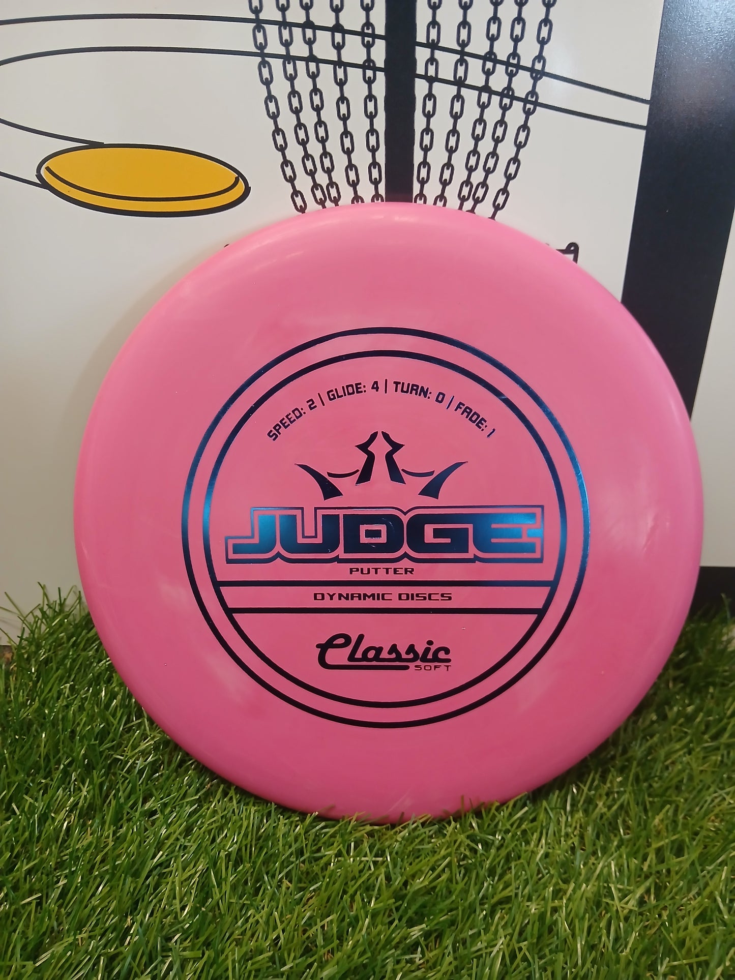 Pink Dynamic Discs Judge putter disc on grass, ideal for disc golf beginners and pros.