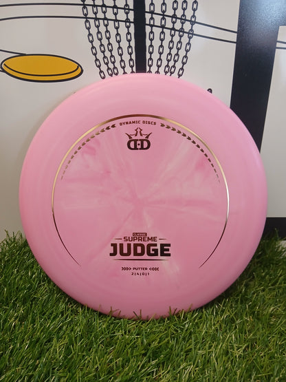 Pink Dynamic Discs Classic Supreme Judge putter disc on grass with chains background