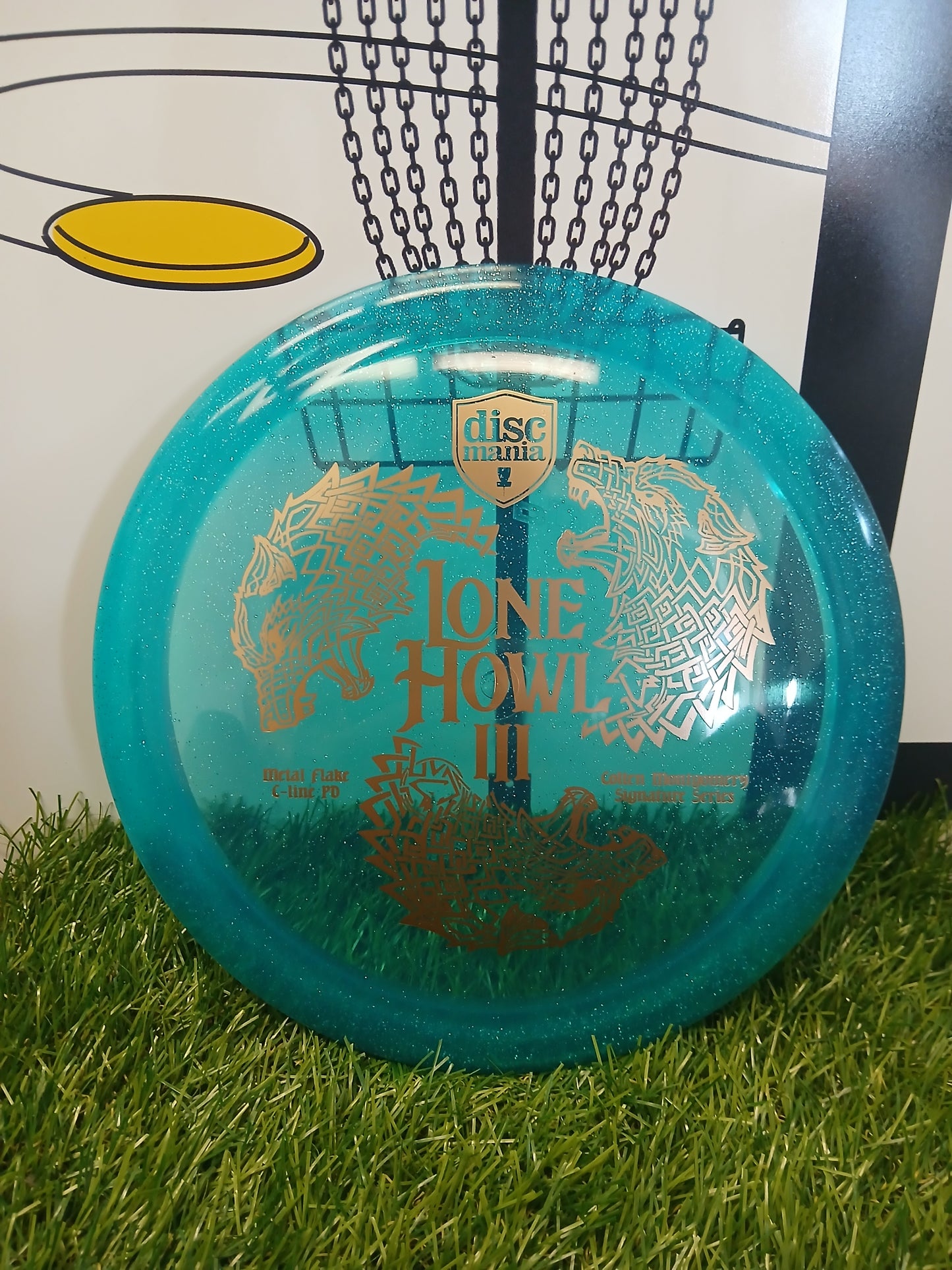 Discmania Lone Howl III disc golf putter on grass, featuring intricate wolf designs and Metal Flake C-line PD plastic.