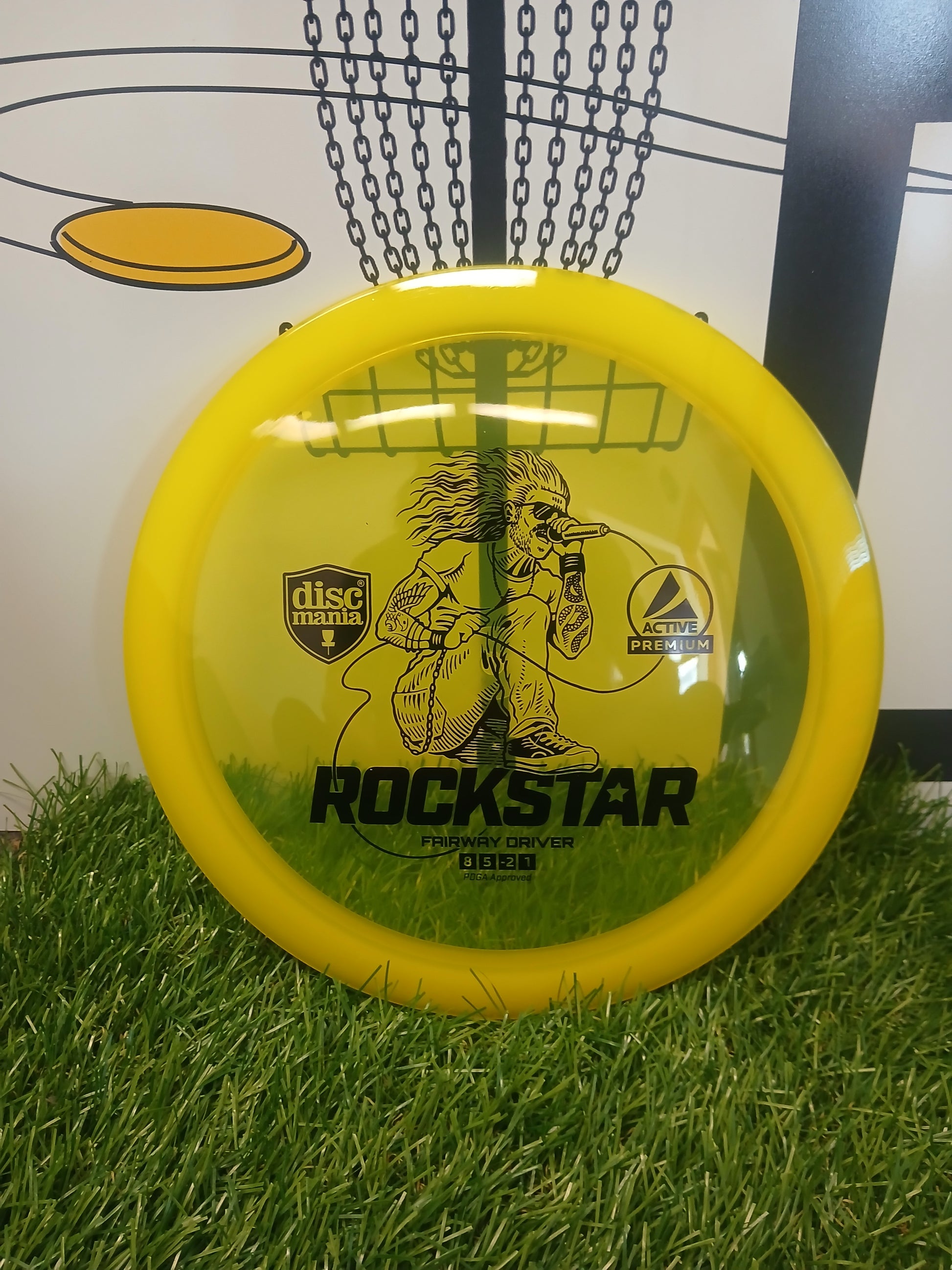 Yellow Discmania Rockstar fairway driver disc golf disc on grass with chains background