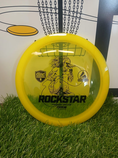 Yellow Discmania Rockstar fairway driver disc golf disc on grass with chains background