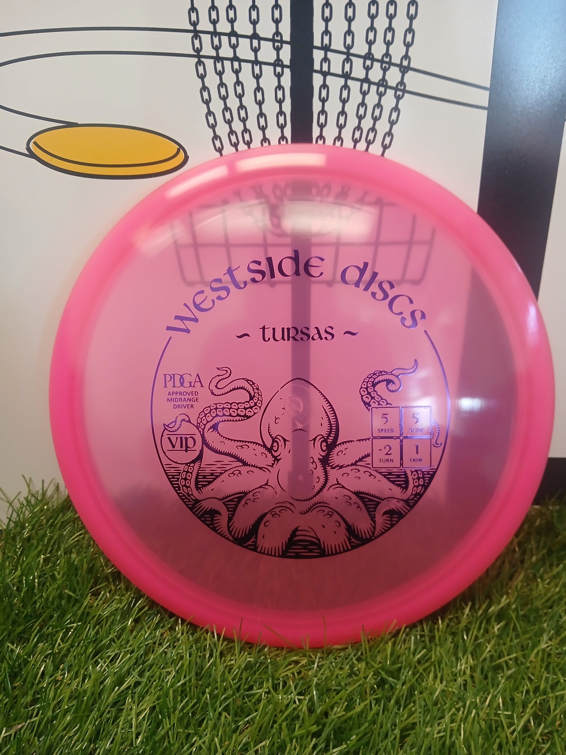 Pink Westside Discs Tursas VIP midrange driver with octopus design, PDGA approved, on grass near basket