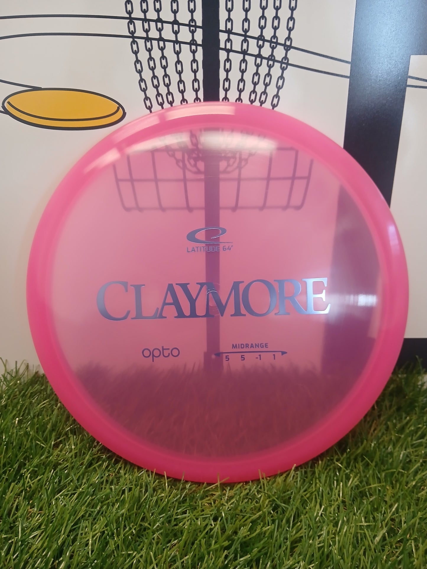 Pink Latitude 64 Claymore Opto midrange disc golf disc on grass, ideal for disc golf enthusiasts.