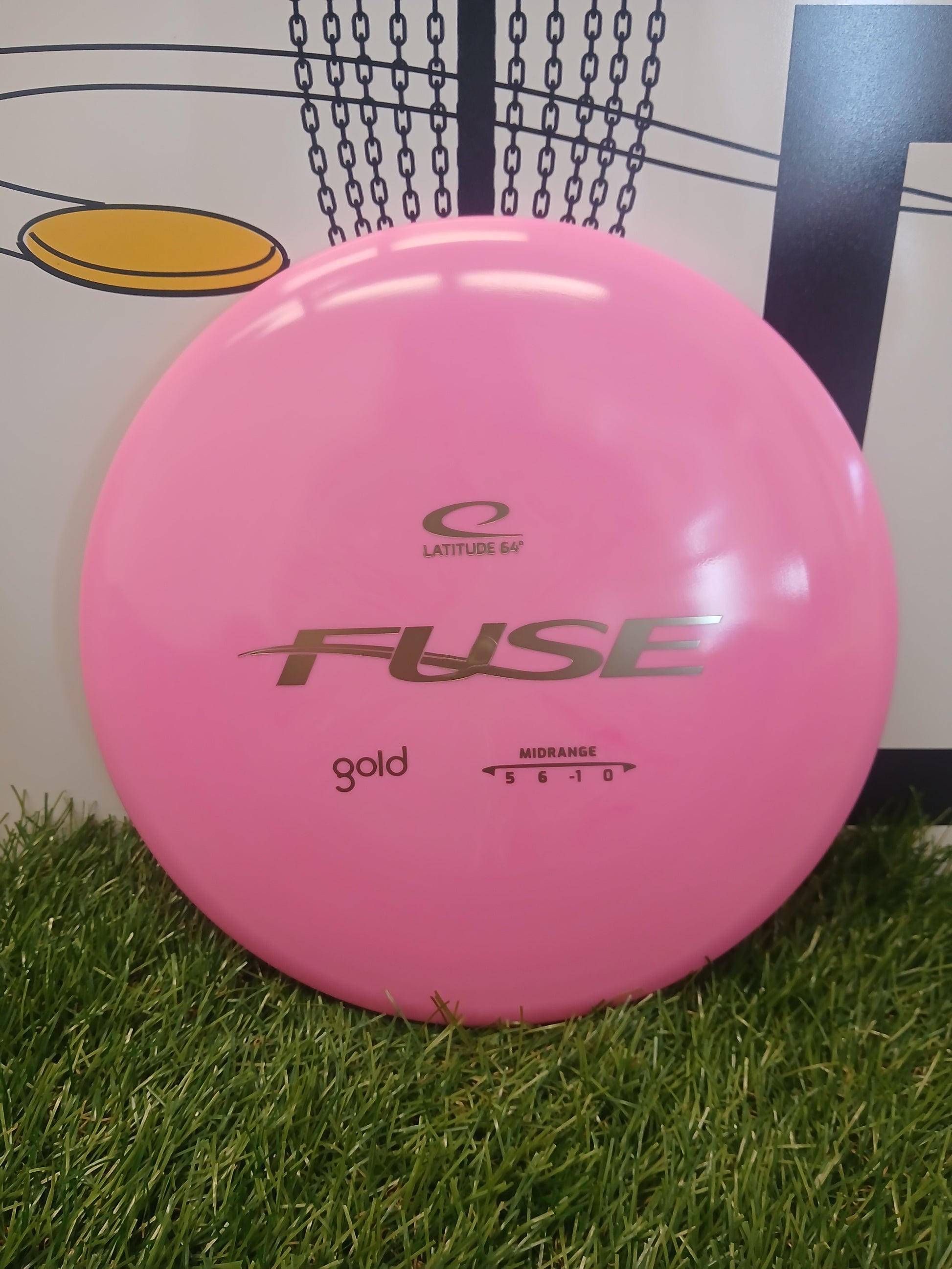 Pink Latitude 64° Fuse Gold midrange disc golf disc on grass, ideal for disc golf enthusiasts.
