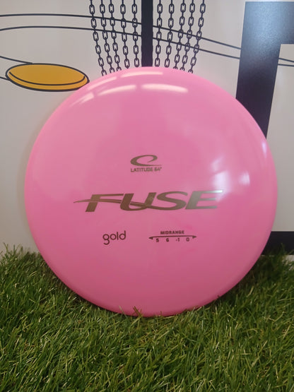 Pink Latitude 64° Fuse Gold midrange disc golf disc on grass, ideal for disc golf enthusiasts.