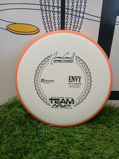 James Conrad 2021 World Champion Envy putter disc, Electron plastic, Team MVP Disc Sports, on grass near basket