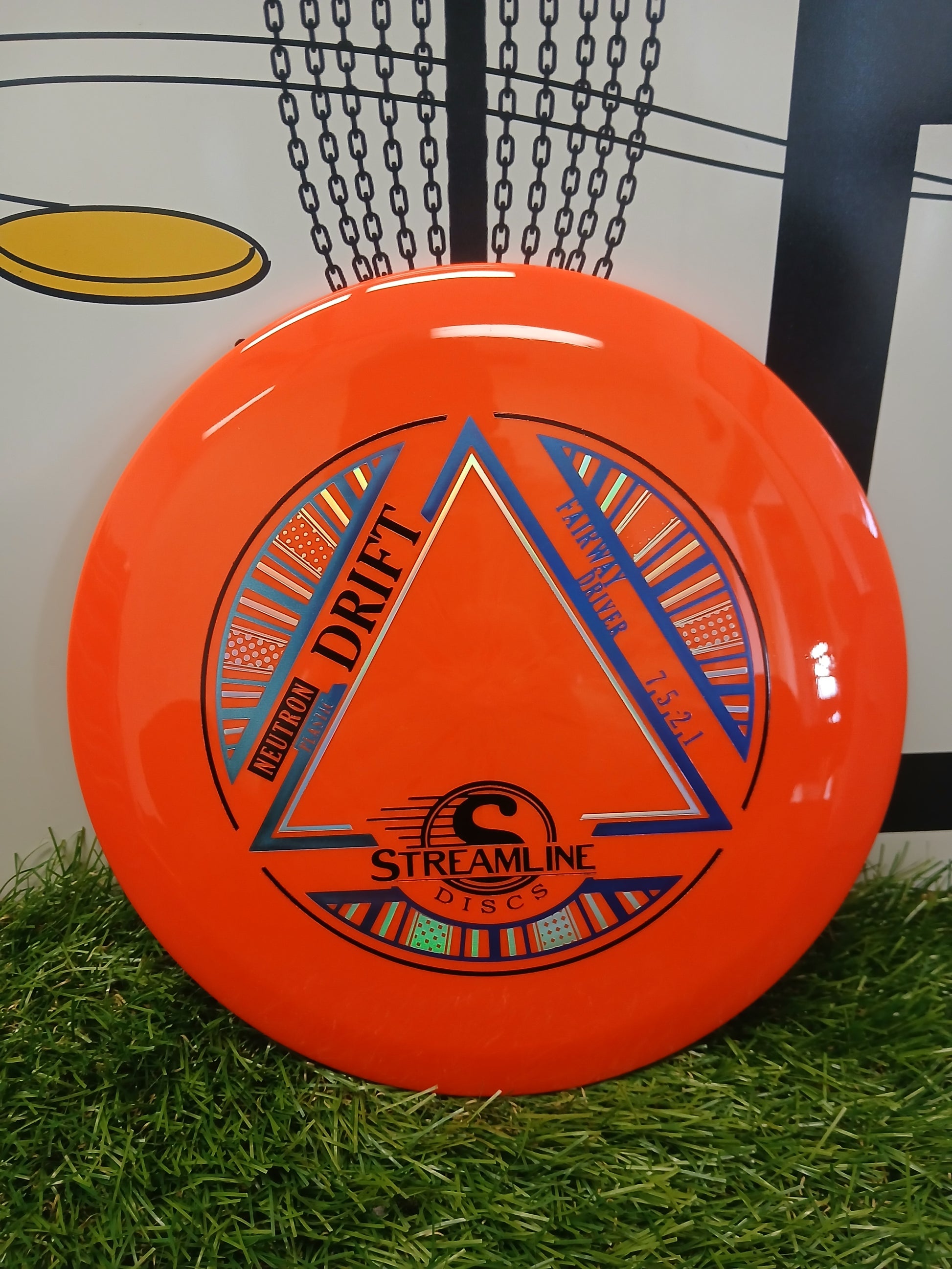 Bright orange Streamline Discs Neutron Drift fairway driver on artificial grass, ideal for disc golf.