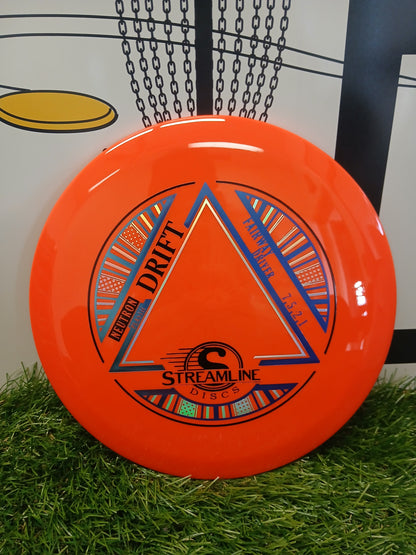 Bright orange Streamline Discs Neutron Drift fairway driver on artificial grass, ideal for disc golf.