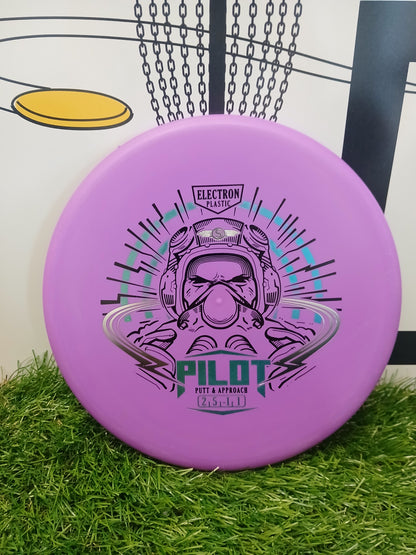 Purple Pilot putter disc golf disc with astronaut graphic, Electron Plastic, on grass near basket