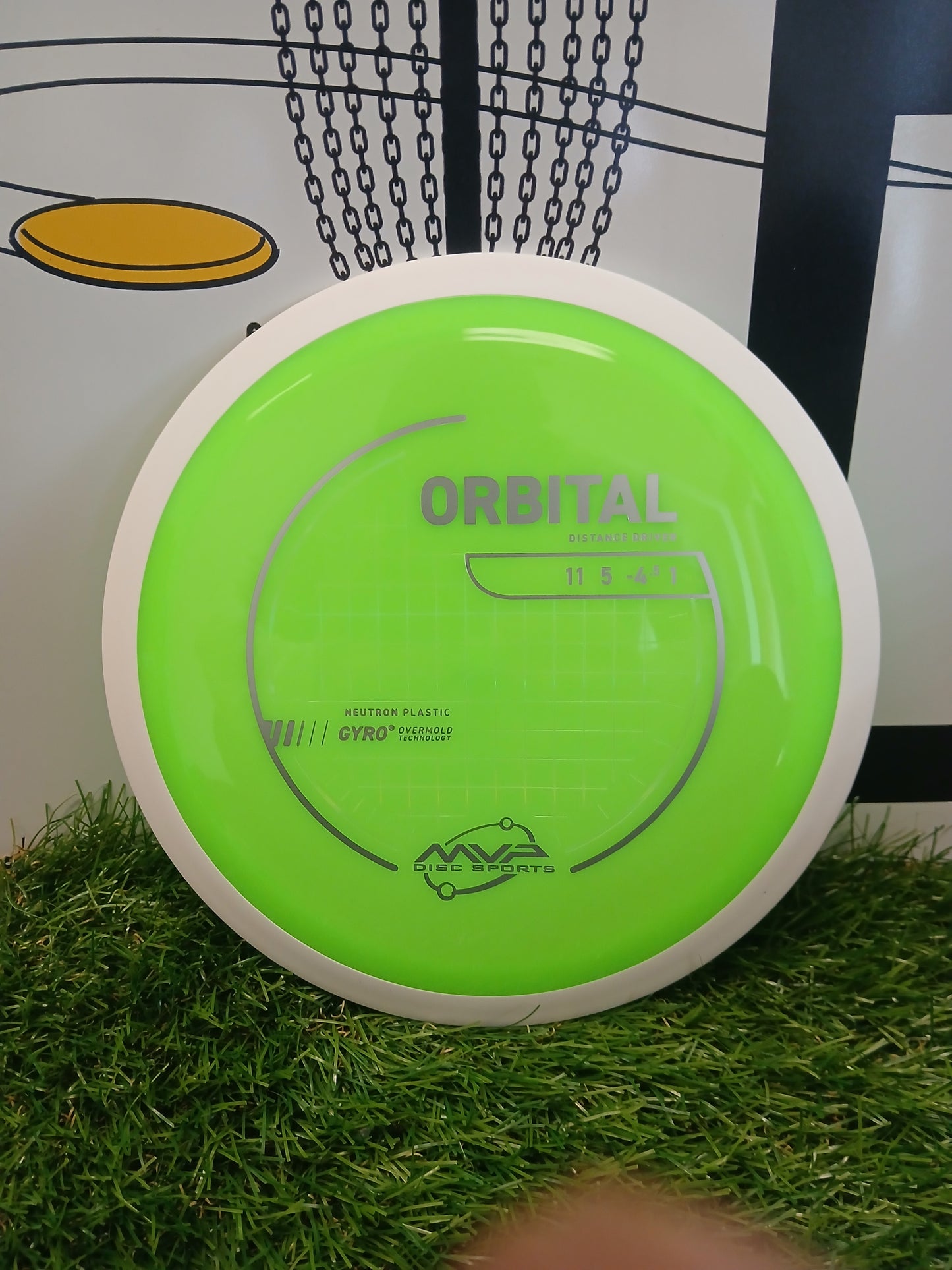 Bright green MVP Disc Sports Orbital distance driver on artificial grass with chain-link backdrop
