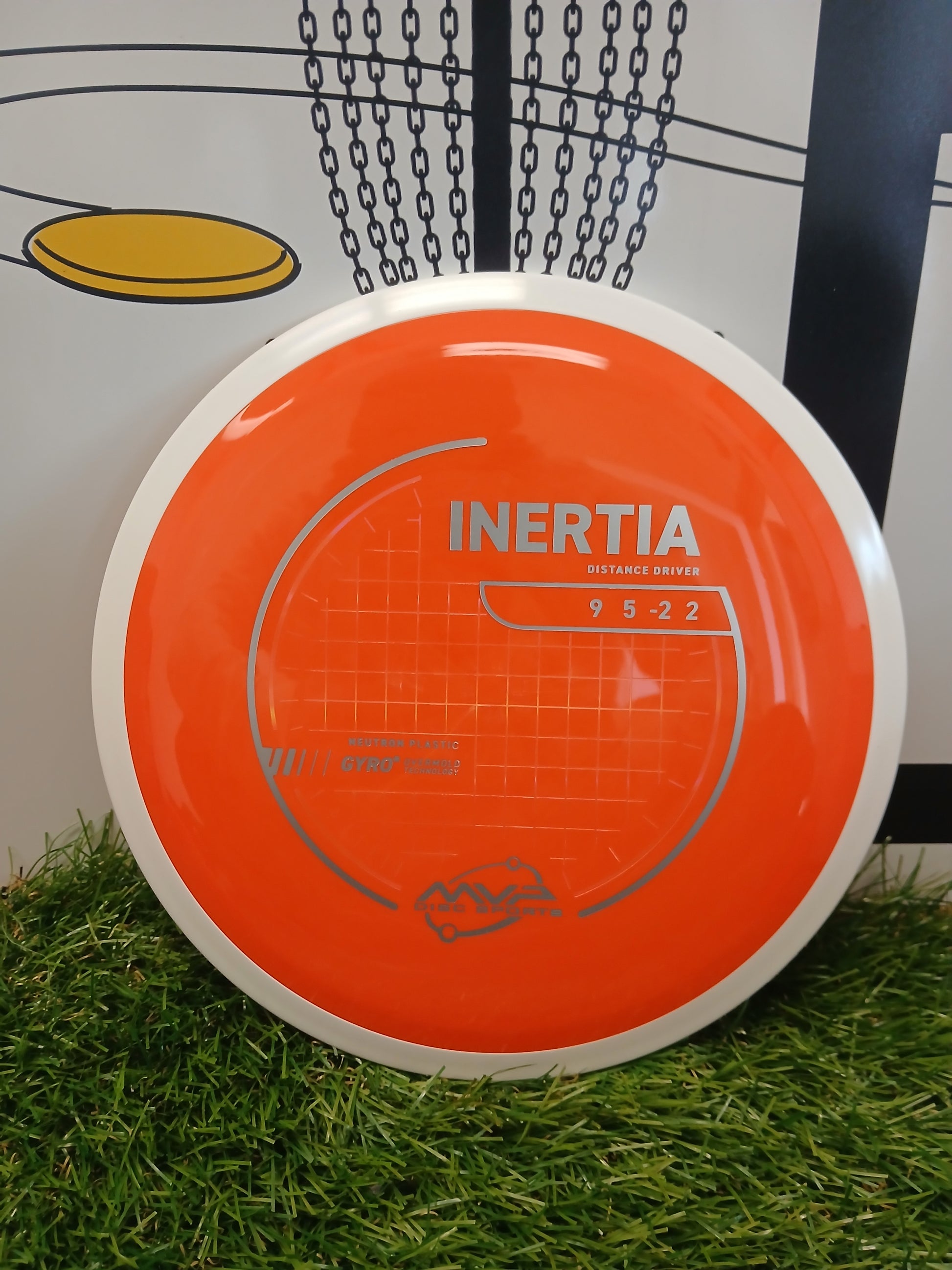 Orange Inertia distance driver disc golf disc on grass, featuring Neutron plastic and Gyro technology
