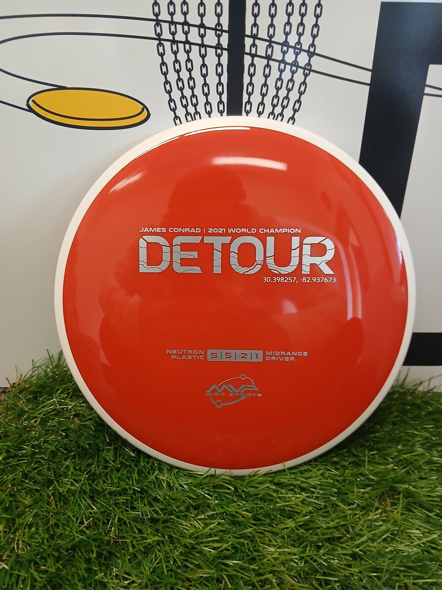 Red MVP Disc Sports Detour midrange driver disc golf disc on grass, James Conrad 2021 World Champion