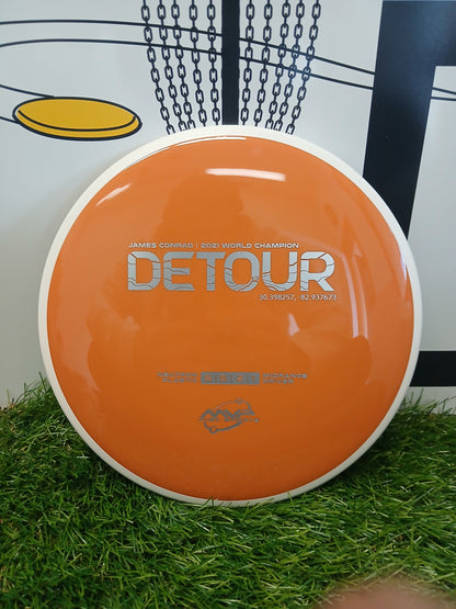 Orange Detour disc golf midrange driver on grass, James Conrad 2021 World Champion edition