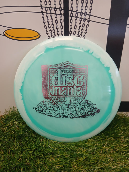 Discmania disc golf disc on grass with chain-link basket background, ideal for disc golf enthusiasts