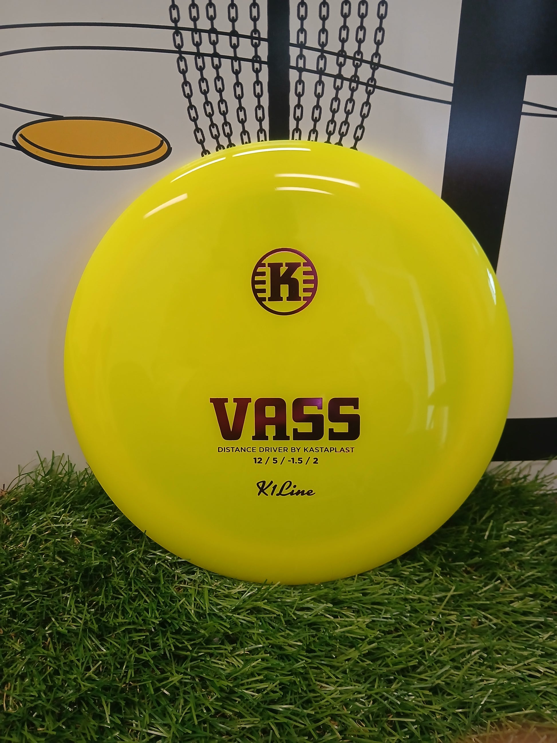 Bright yellow Kastaplast Vass distance driver disc golf disc on artificial grass, ideal for long throws.