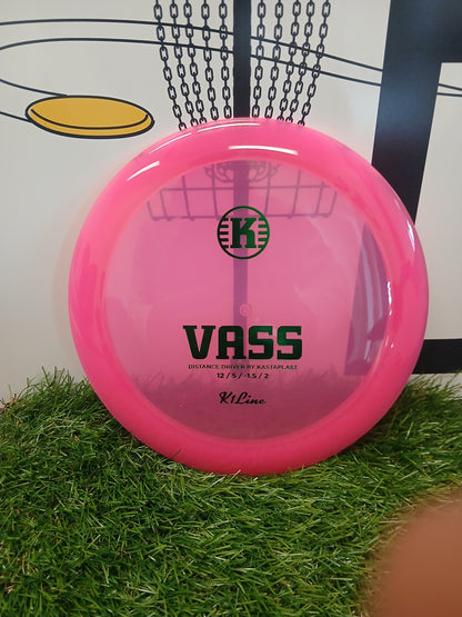 Pink Kastaplast Vass distance driver disc golf disc on grass with basket graphic