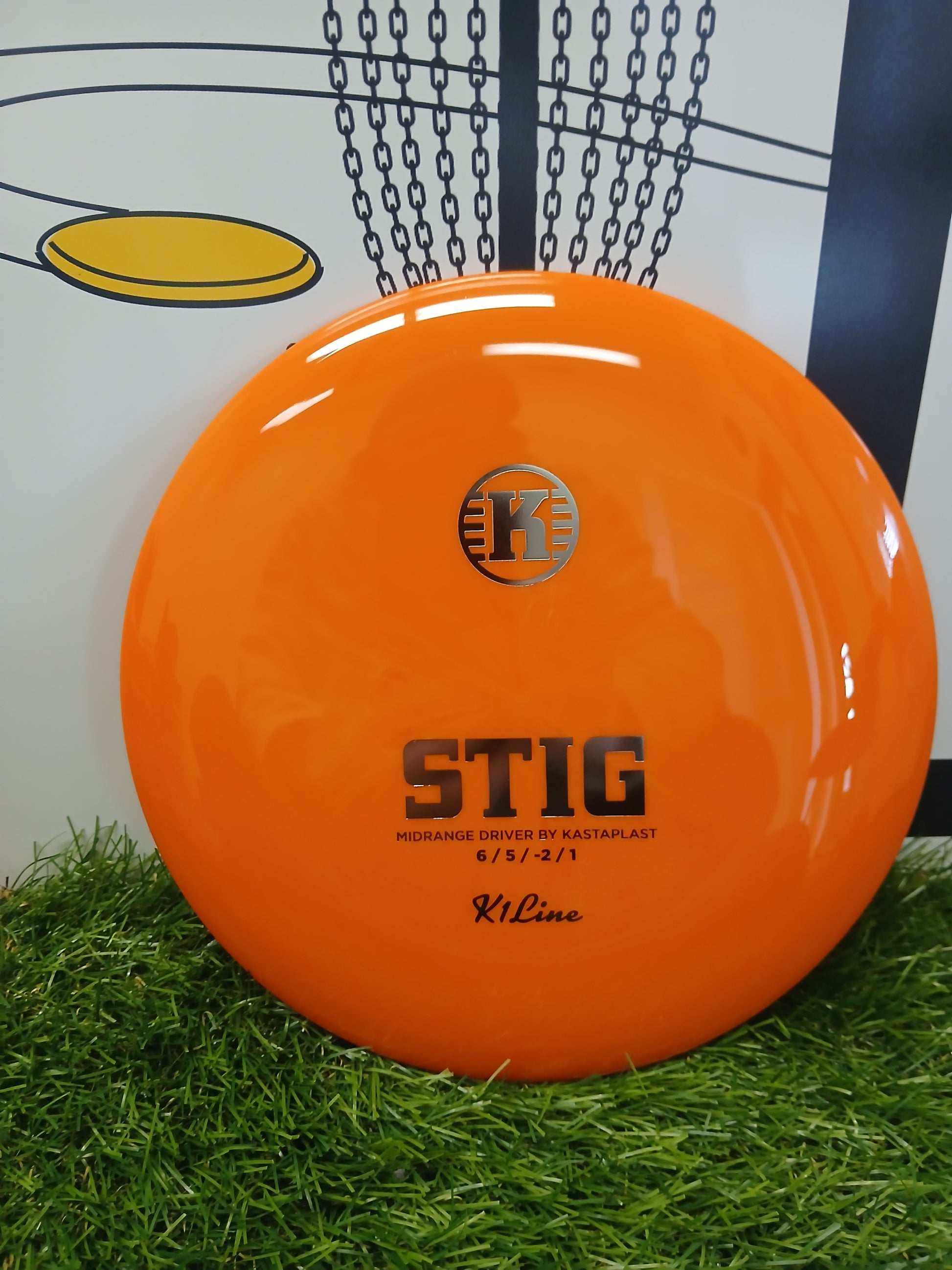 Bright orange Kastaplast Stig midrange disc golf driver on artificial grass, ideal for disc golf enthusiasts.