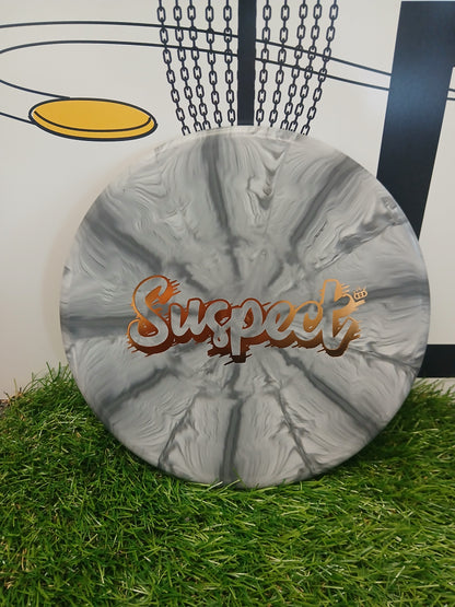 Suspect disc golf disc with gray marble design, resting on grass near a basket