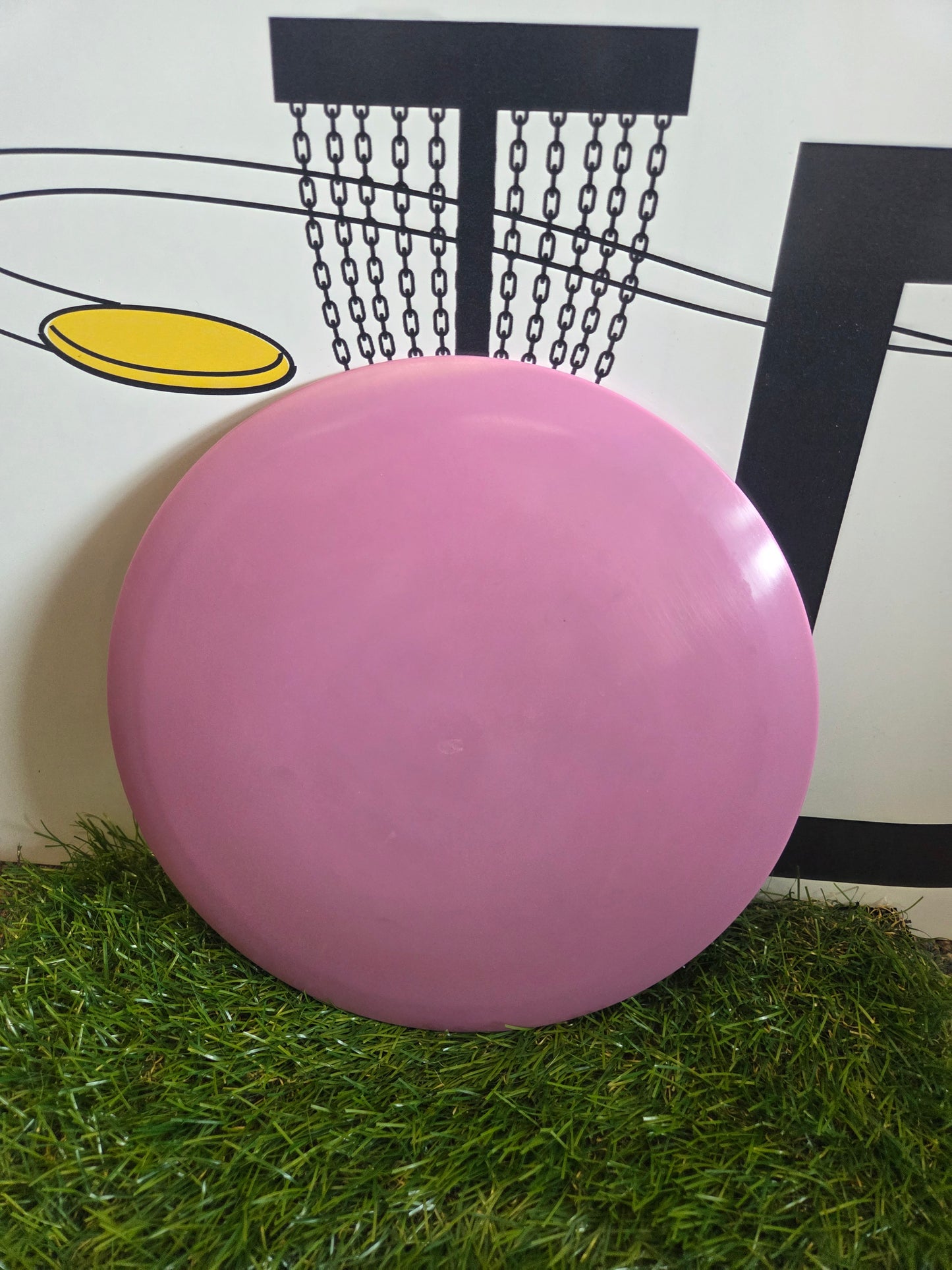 Pink disc golf disc on green turf with basket graphic background