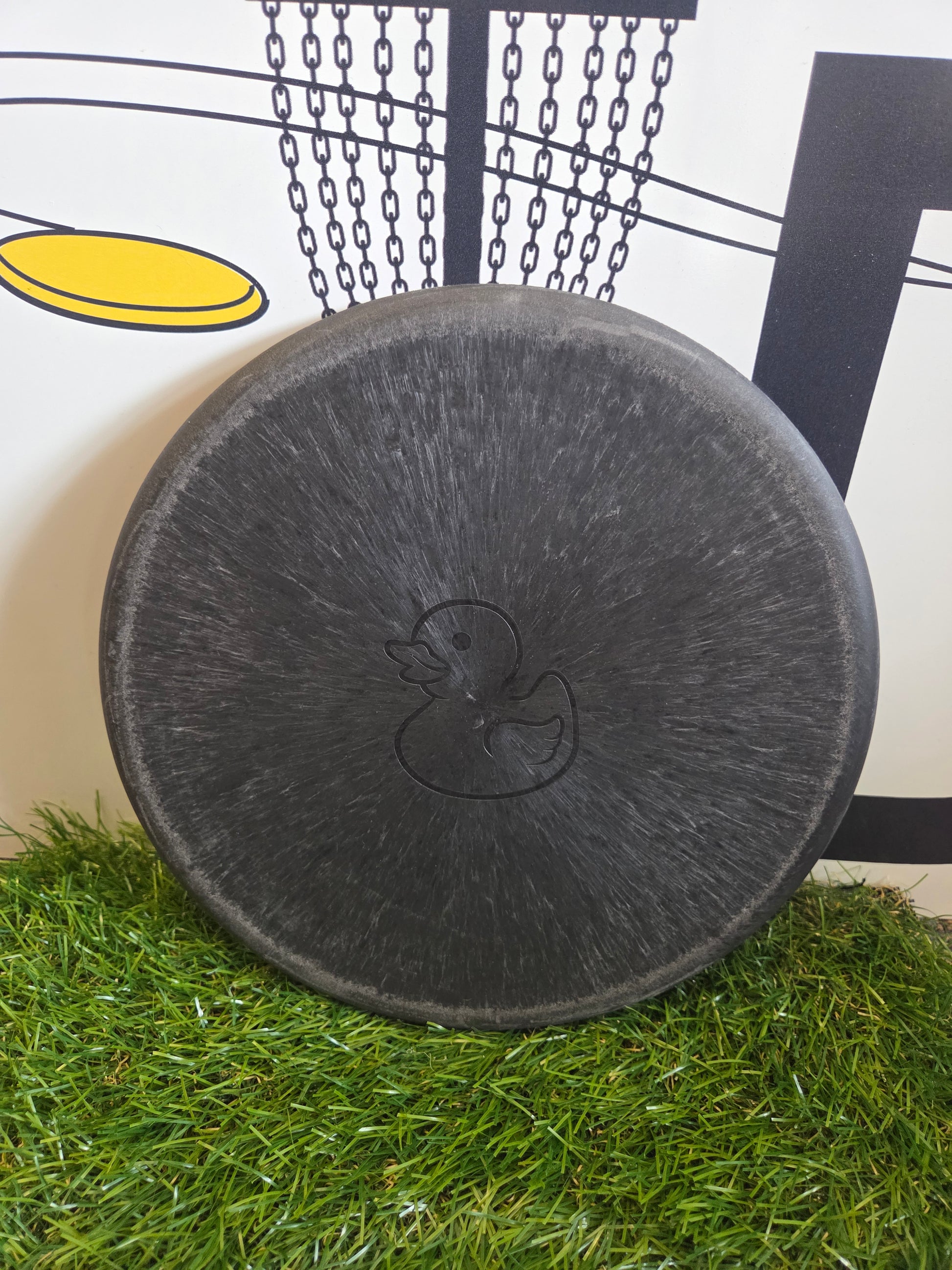 Black disc golf disc with duck logo on artificial grass, perfect for disc golf enthusiasts.