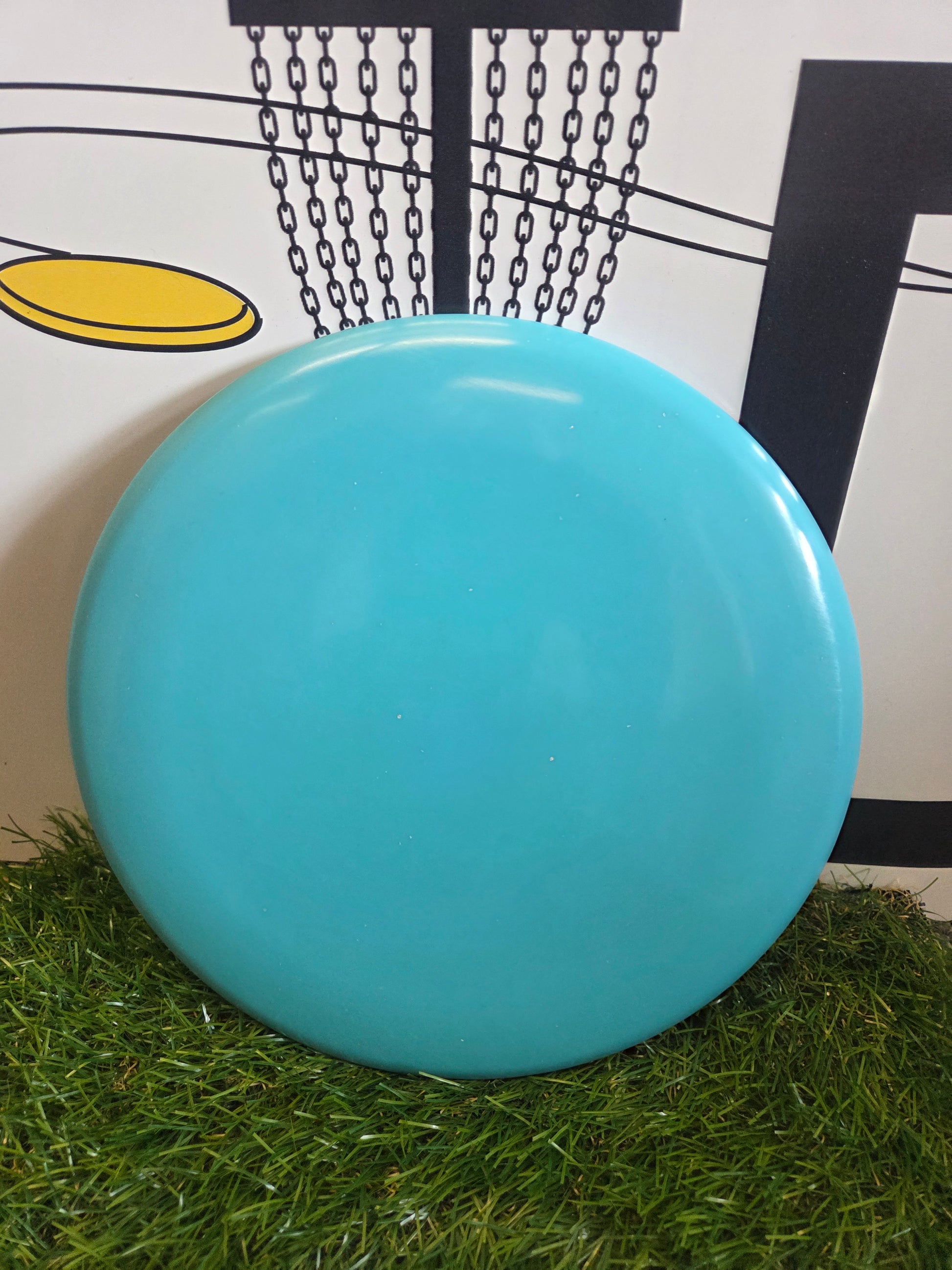 Bright blue disc golf disc on artificial grass with chain basket background