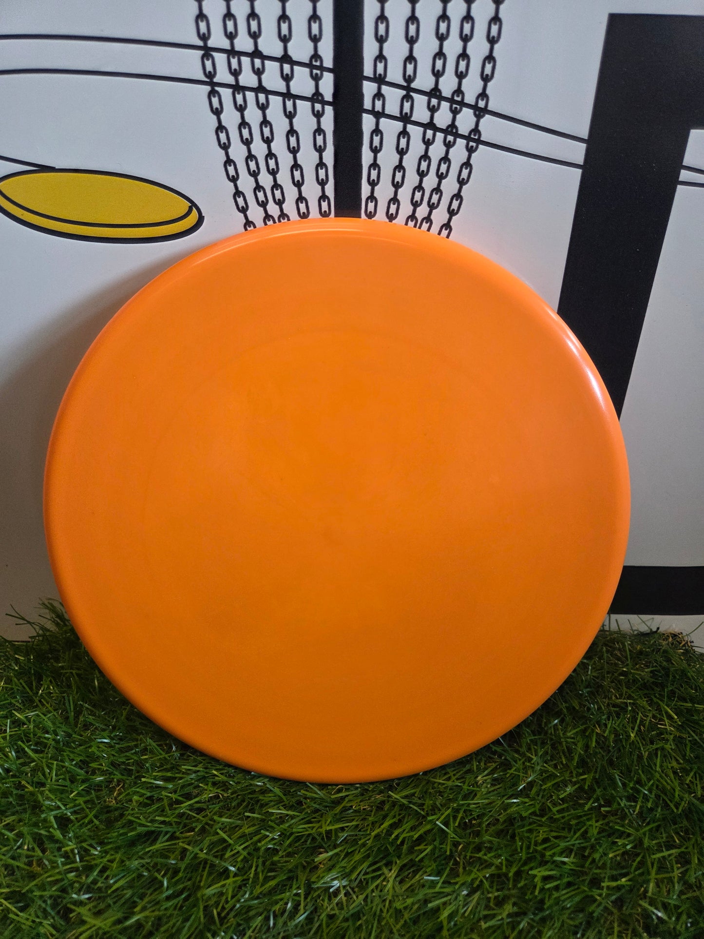Bright orange disc golf disc on green grass with chain basket background