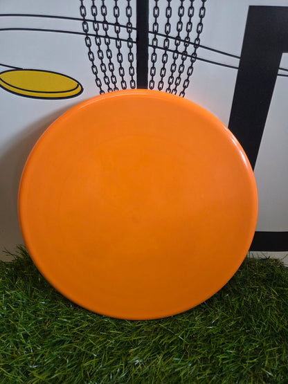 Bright orange disc golf disc on green grass with chain basket background