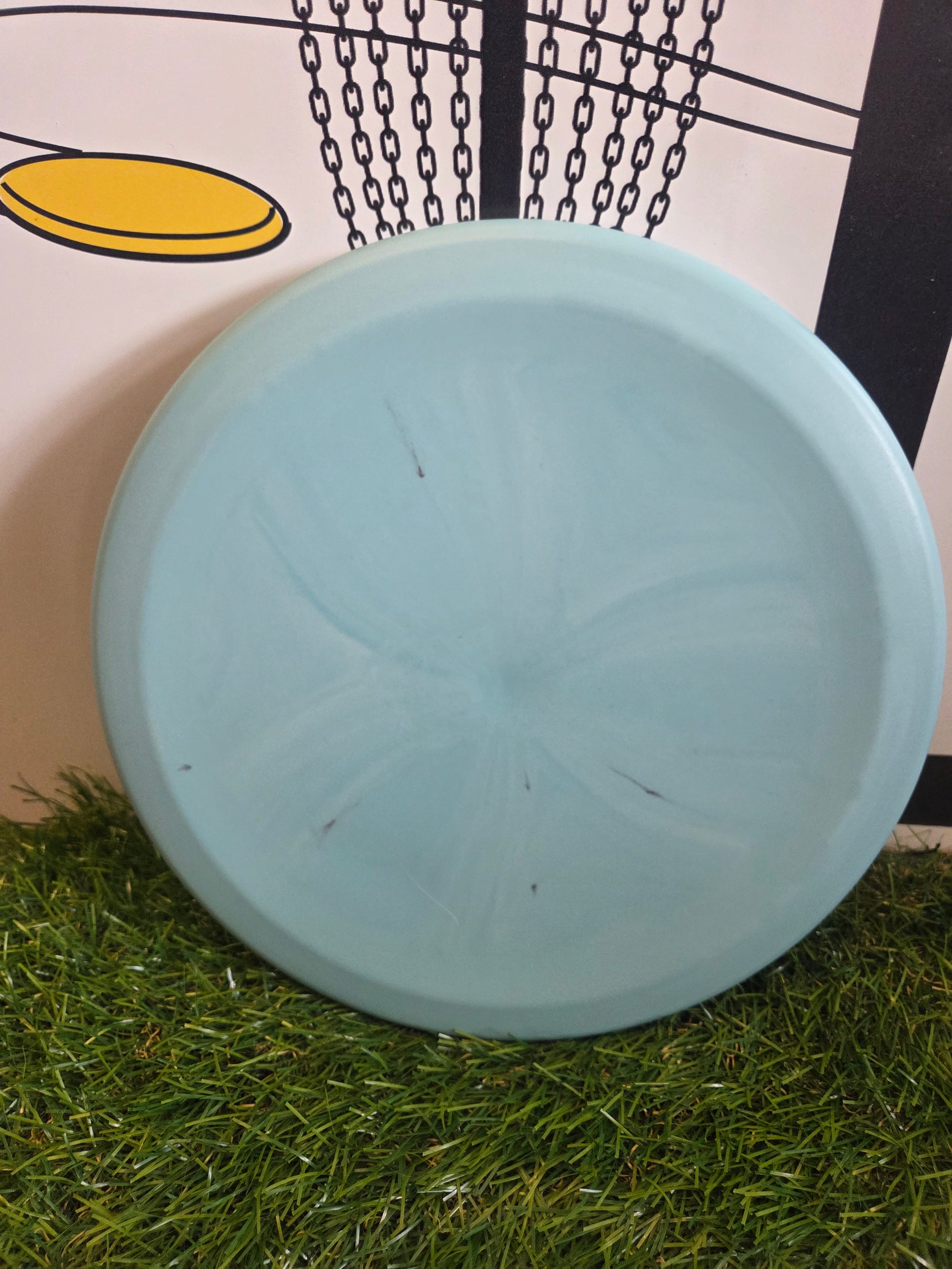 Light blue disc golf disc on artificial grass with chain basket background