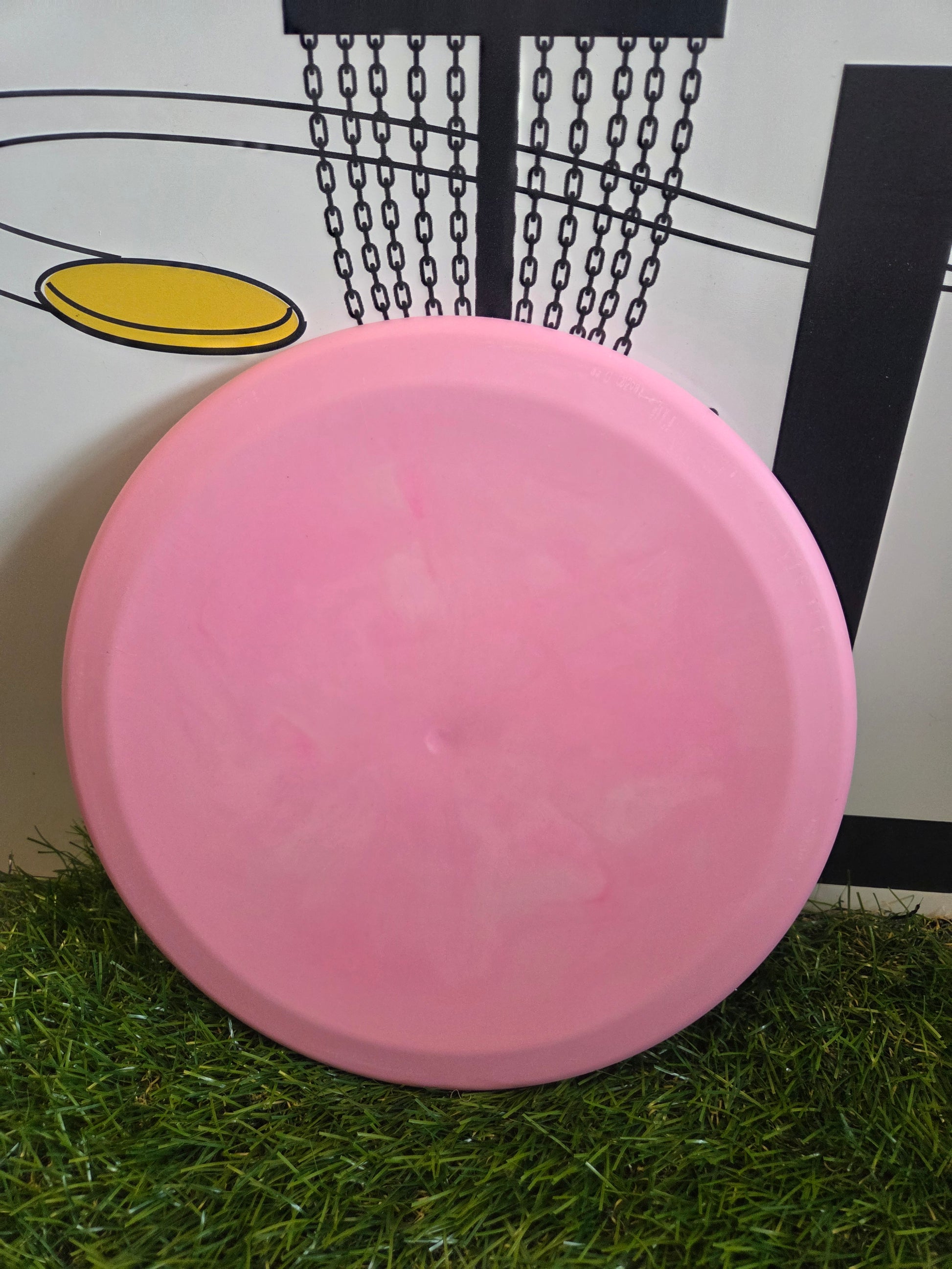 Pink disc golf disc on grass with basket background