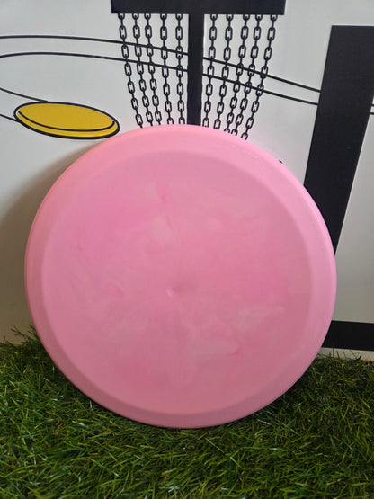 Pink disc golf disc on grass with basket background
